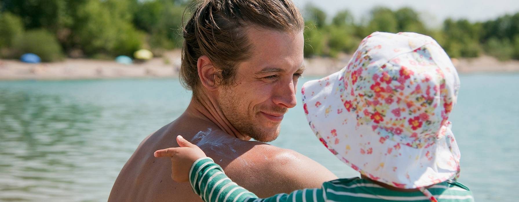 Papà tiene in braccio bambina con cappellino al mare
