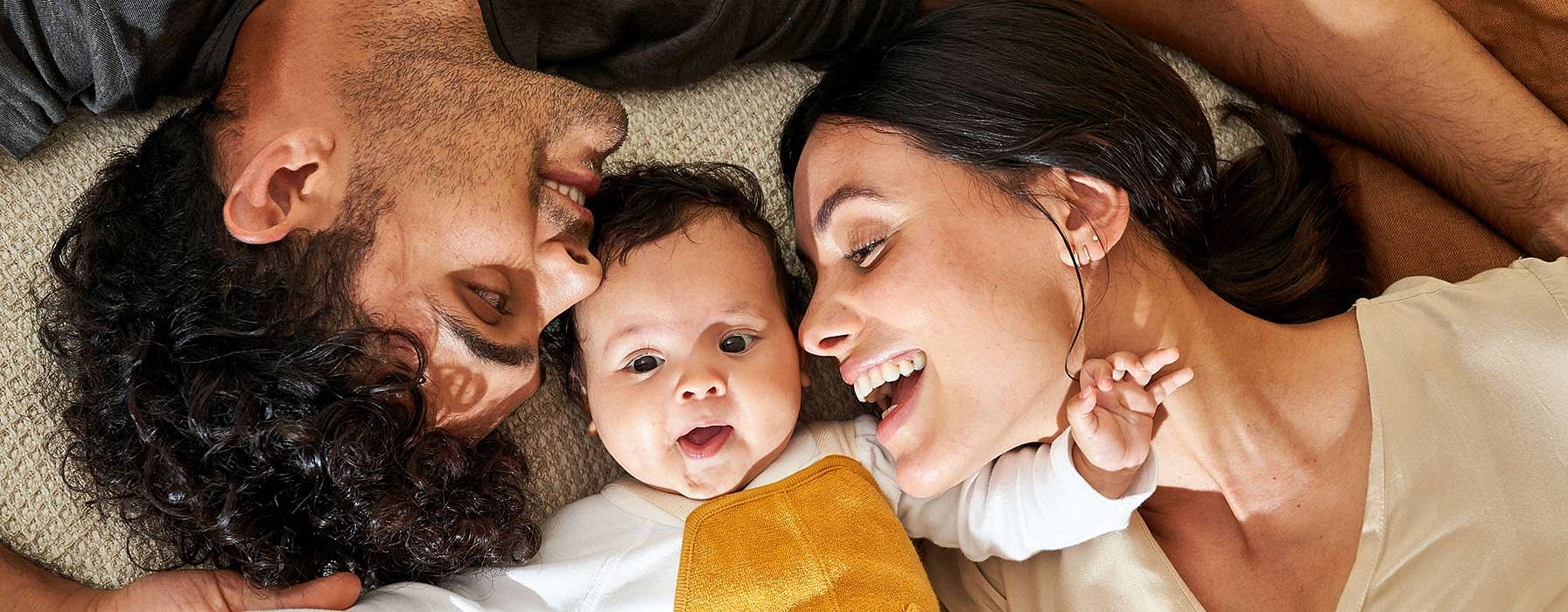 Mamma e papà e bimbo neonato sdraiati sorridono e si guardano