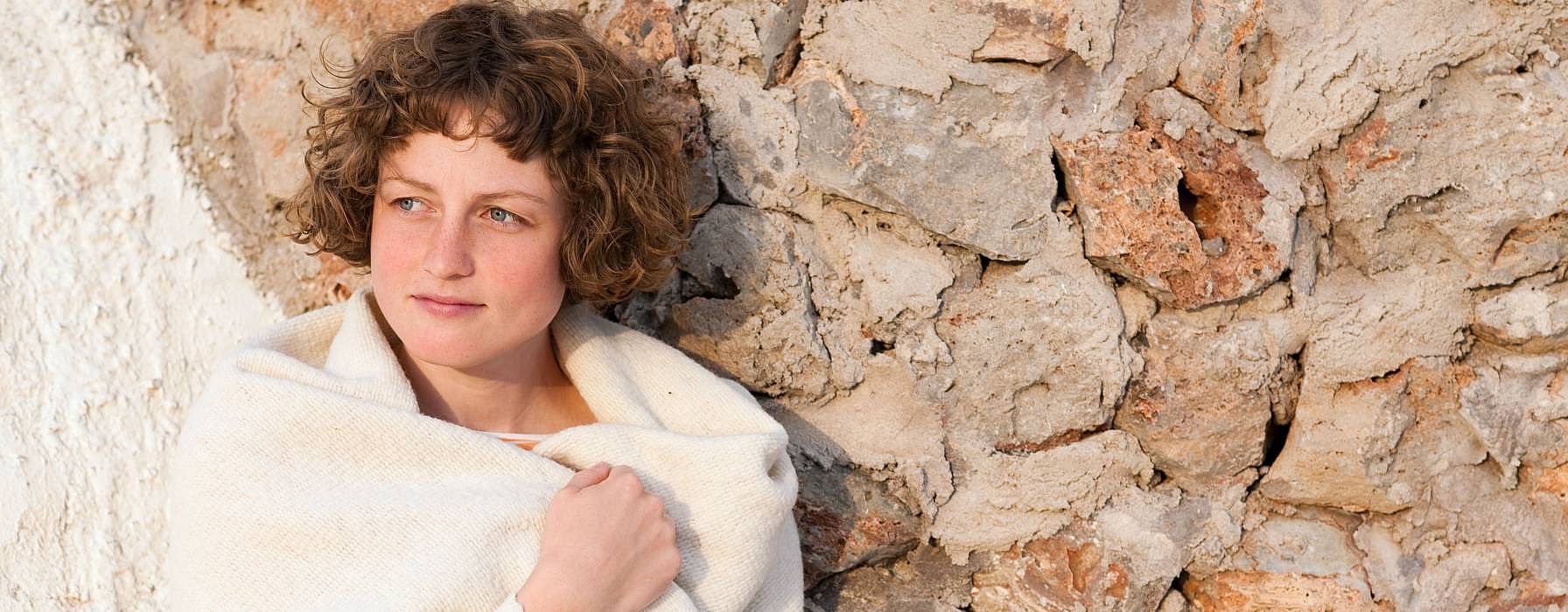 ragazza con sciarpa appoggiata ad un muro in pietra