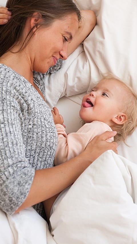 Bambino e mamma a letto, il bambino fa la linguaccia alla mamma che sorride