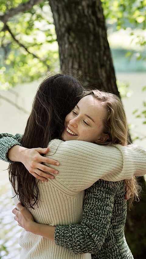 Due donne si abbracciano vicino ad un albero