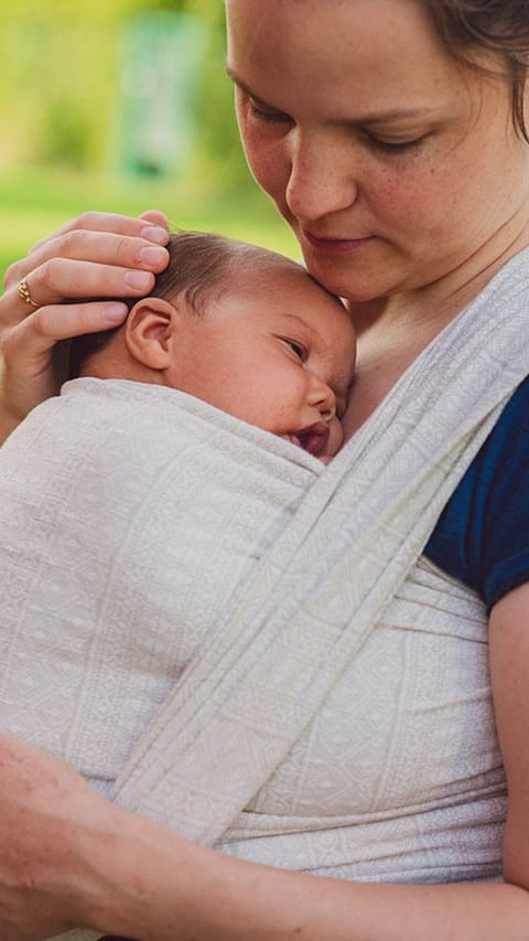 Mamma tiene il neonato in una fascia e poggia la mano sulla sua testolina