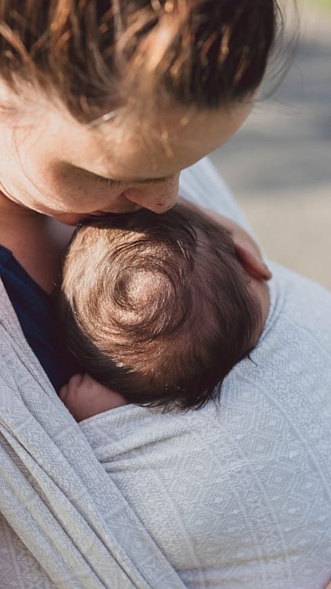 Mamma bacia la testa del suo neonato mentre è in una fascia