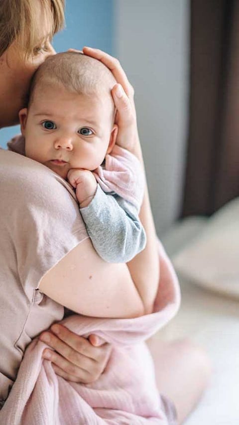 Mamma tiene in braccio neonato appoggiando una mano sulla sua testa