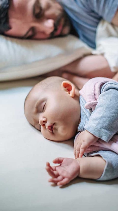 Neonato dorme e sullo sfondo il papà dorme
