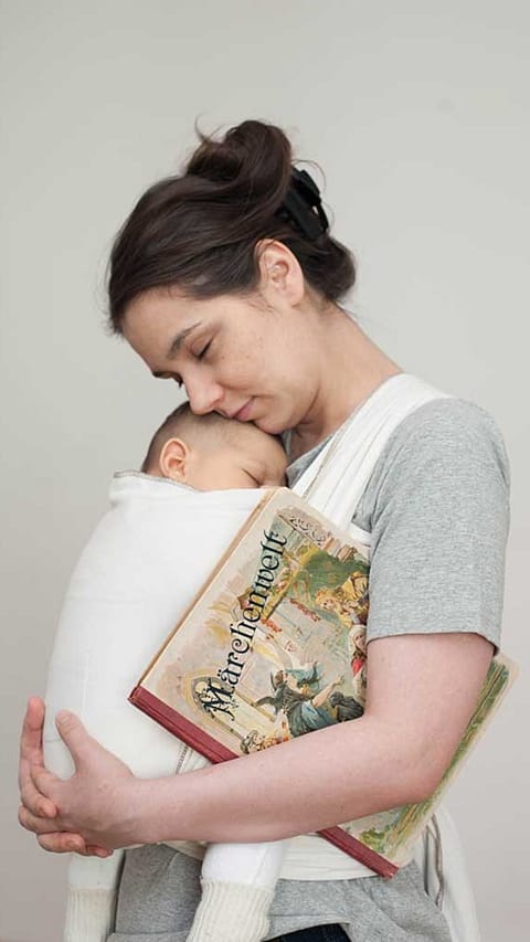 Mamma tiene in braccio un neonato mentre lui dorme, lei appoggia la guancia sulla sua testa