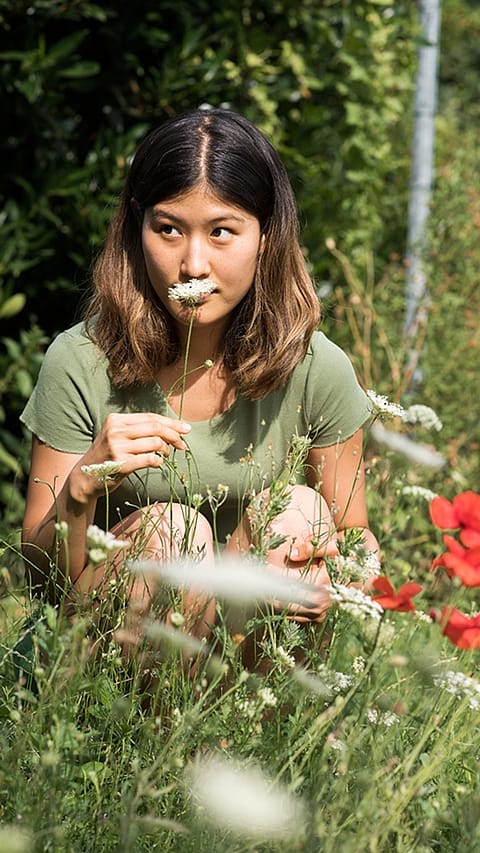 Donna accovacciata in natura annusa un fiore bianco