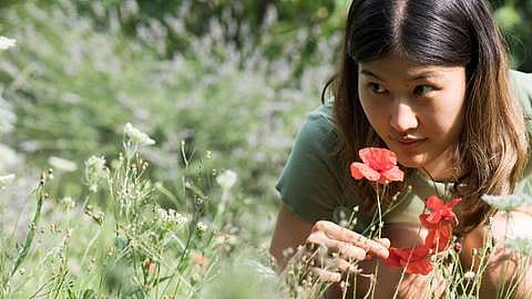 ragazza in un campo che annusa un papavero