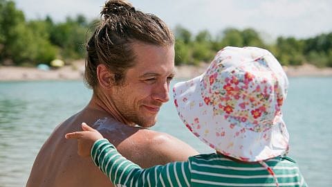 Papà tiene in braccio bambina con cappellino al mare