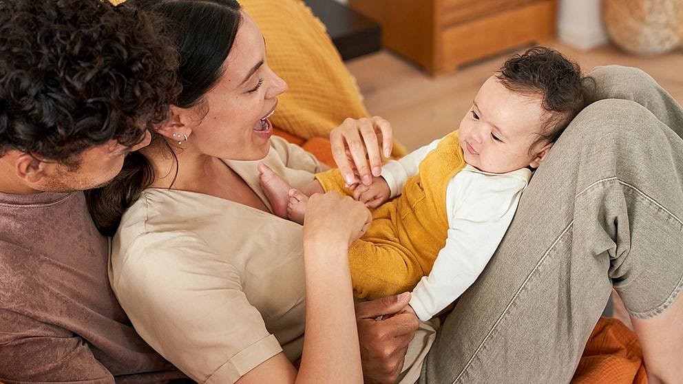 Mamma gioca con il neonato mentre è sulle sue gambe e viene abbracciata dal papà del neonato