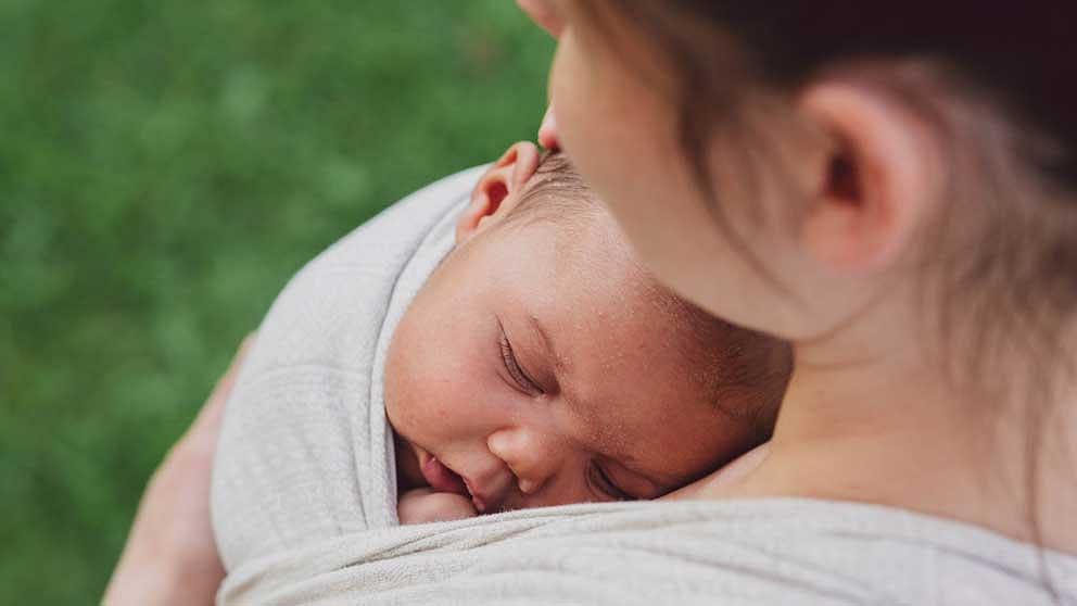 Inquadratura dall'alto di un neonato che dorme in braccio alla mamma in una fascia