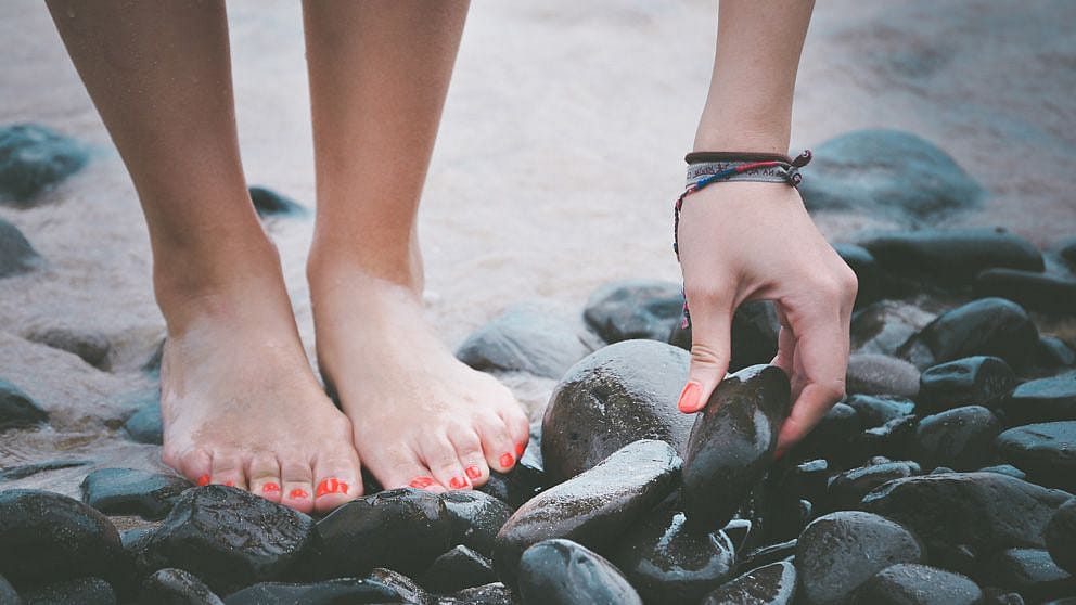 Mano femminile raccoglie un sasso da terra sulla spiaggia
