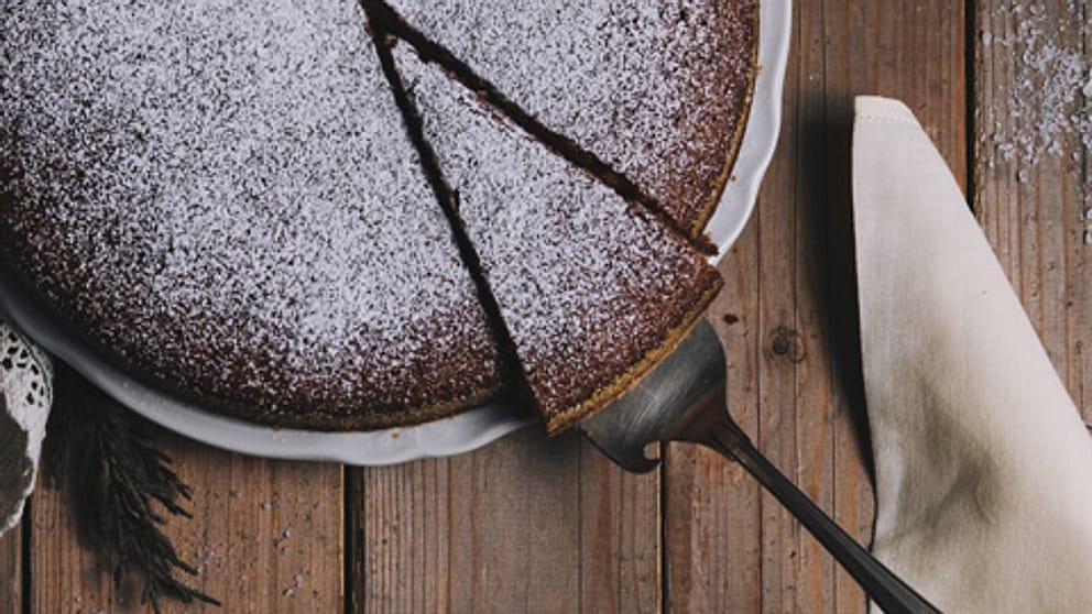 Una sacher con zucchero a velo mentre un pezzo viene tagliato